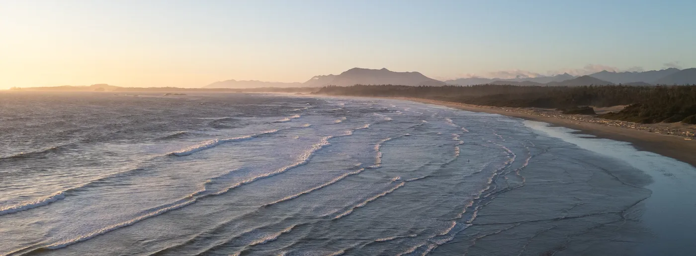 Golden evening light over Long Beach, Tofino, with Pacific surf and forested mountains